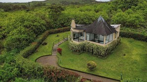 Une maison moderne dotée d’une véranda en verre, entourée d’une végétation luxuriante et bordée d’un sentier sinueux.