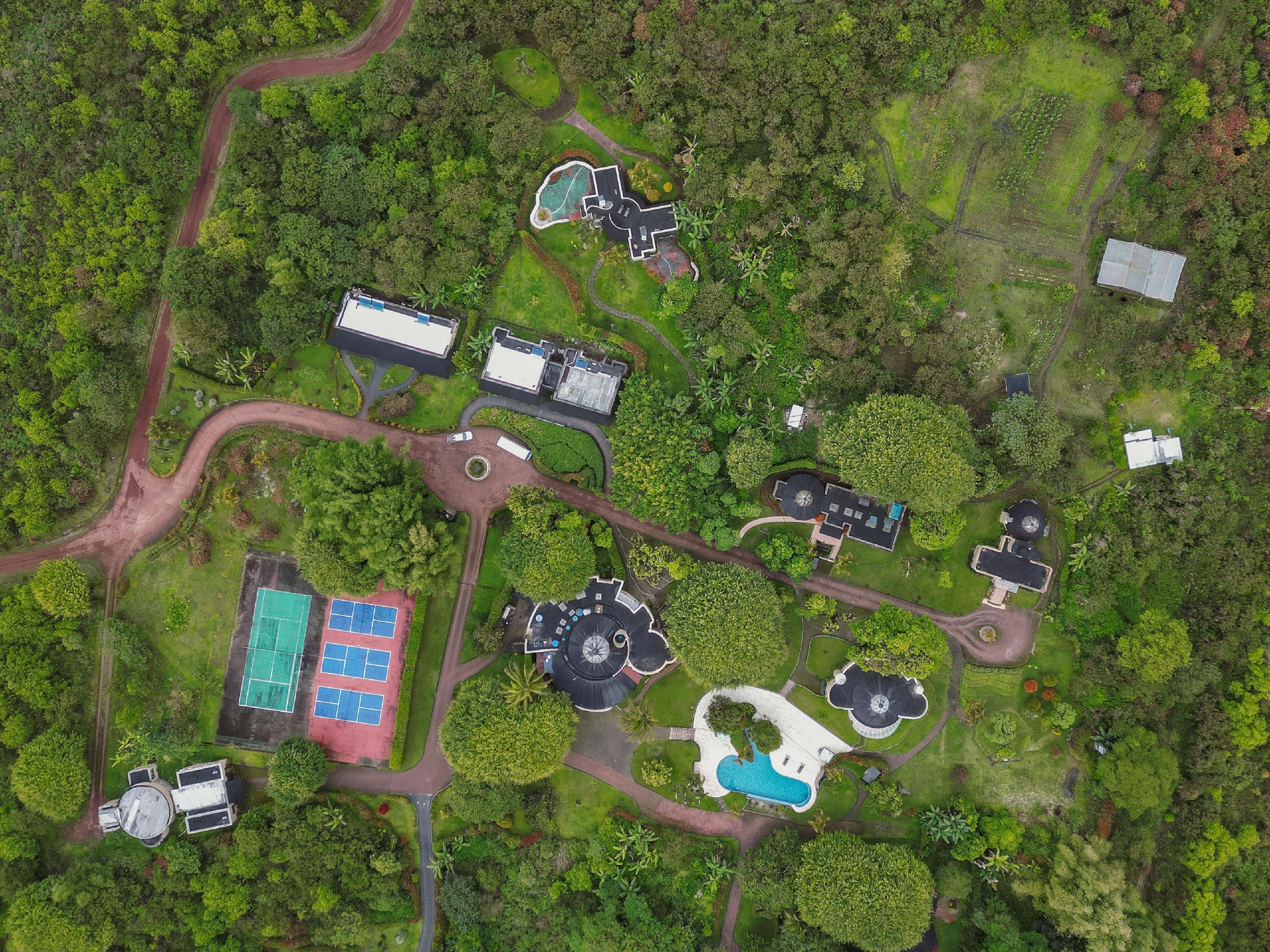 Vista aérea de un complejo turístico con varias edificaciones, una piscina y jardines cuidados.