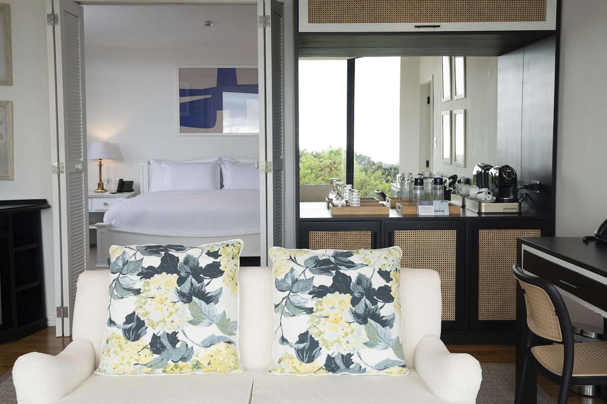 A hotel room with a bed, a desk with a telephone, a coffee station, and a view of greenery.