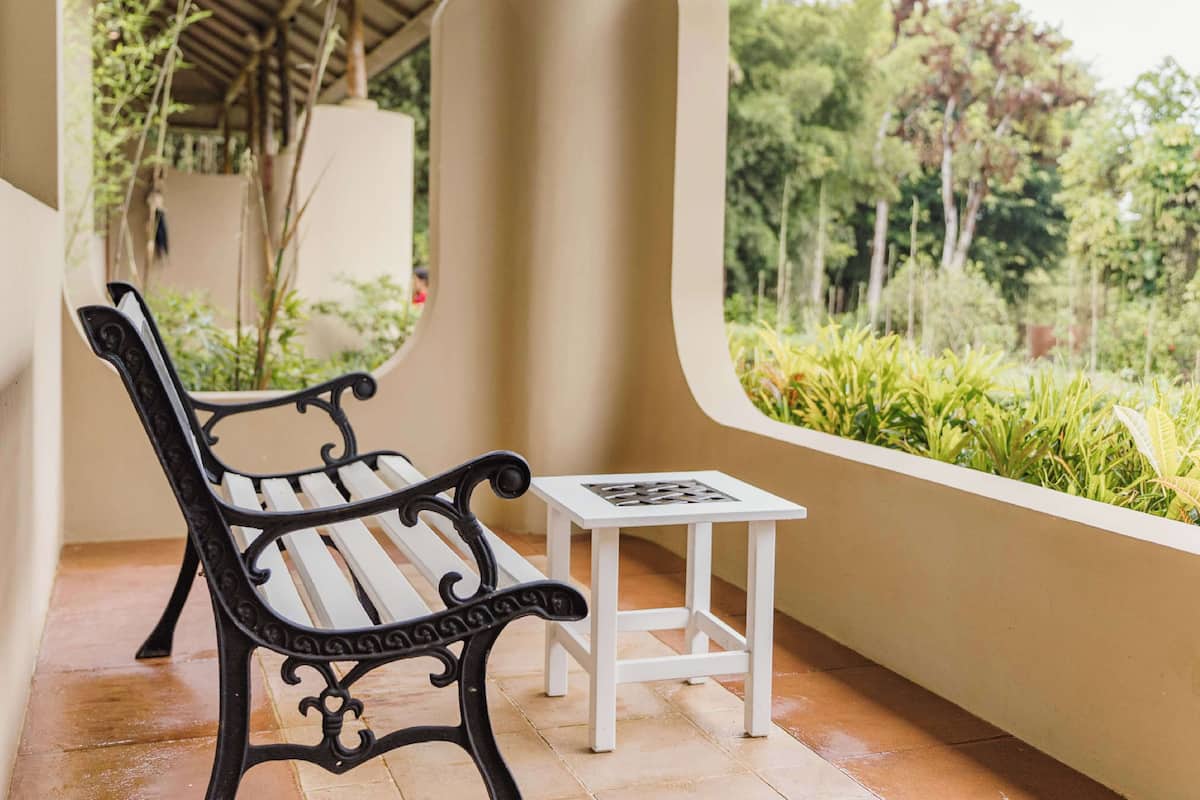 A bench and a small table on a balcony with a view of greenery.