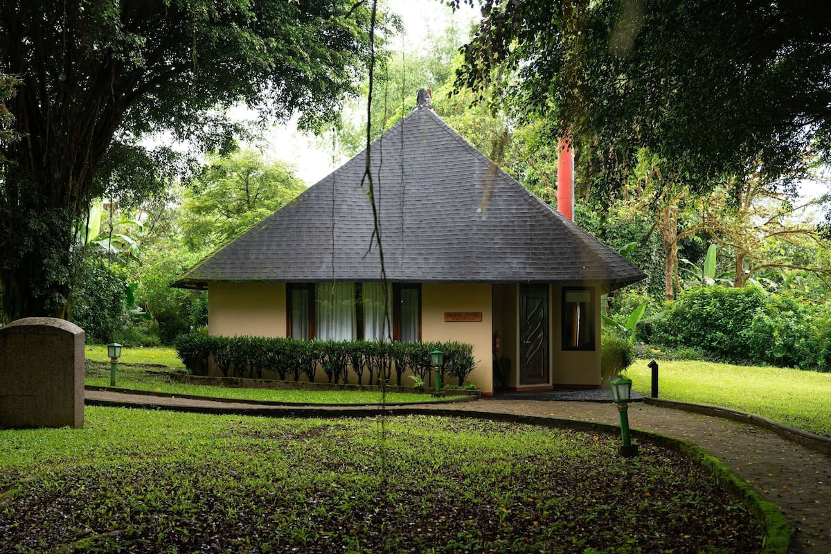 A small, single-story building with a steeply pitched roof, surrounded by lush greenery and a well-maintained lawn.