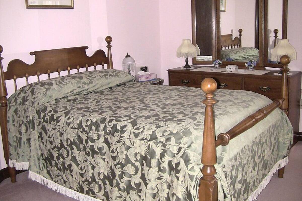 A bedroom with a wooden bed, a dresser, a mirror, and a framed picture on the wall.
