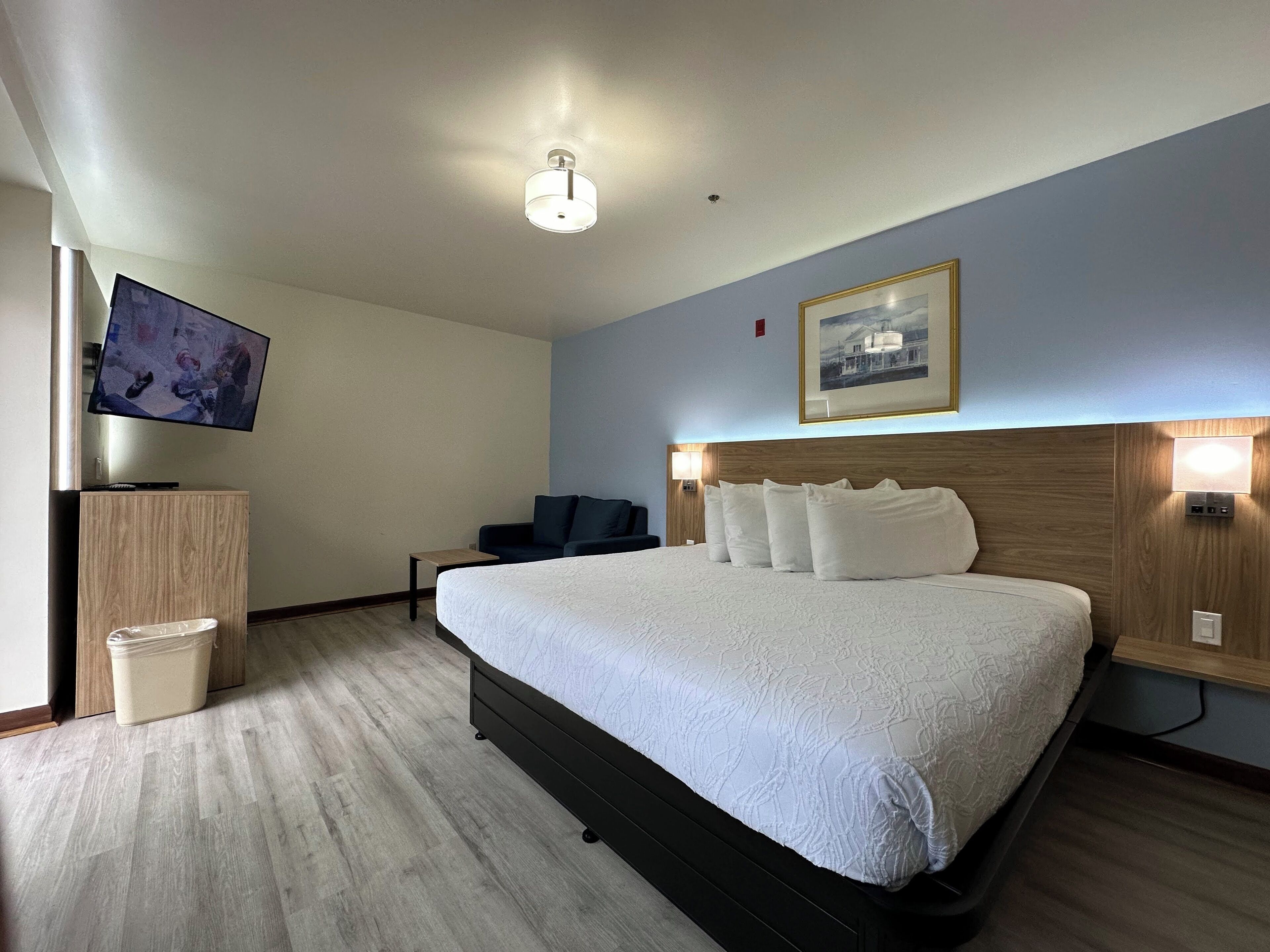 A hotel room with a large bed, a TV mounted on the wall, a desk, and a chair.