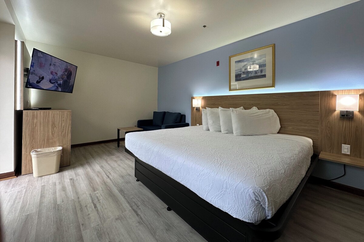 Una habitación de hotel con una cama grande, un televisor en la pared, un escritorio y una silla.