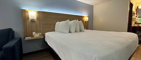 A hotel room with a large bed, a bedside table with a lamp, a chair, and a wooden headboard.