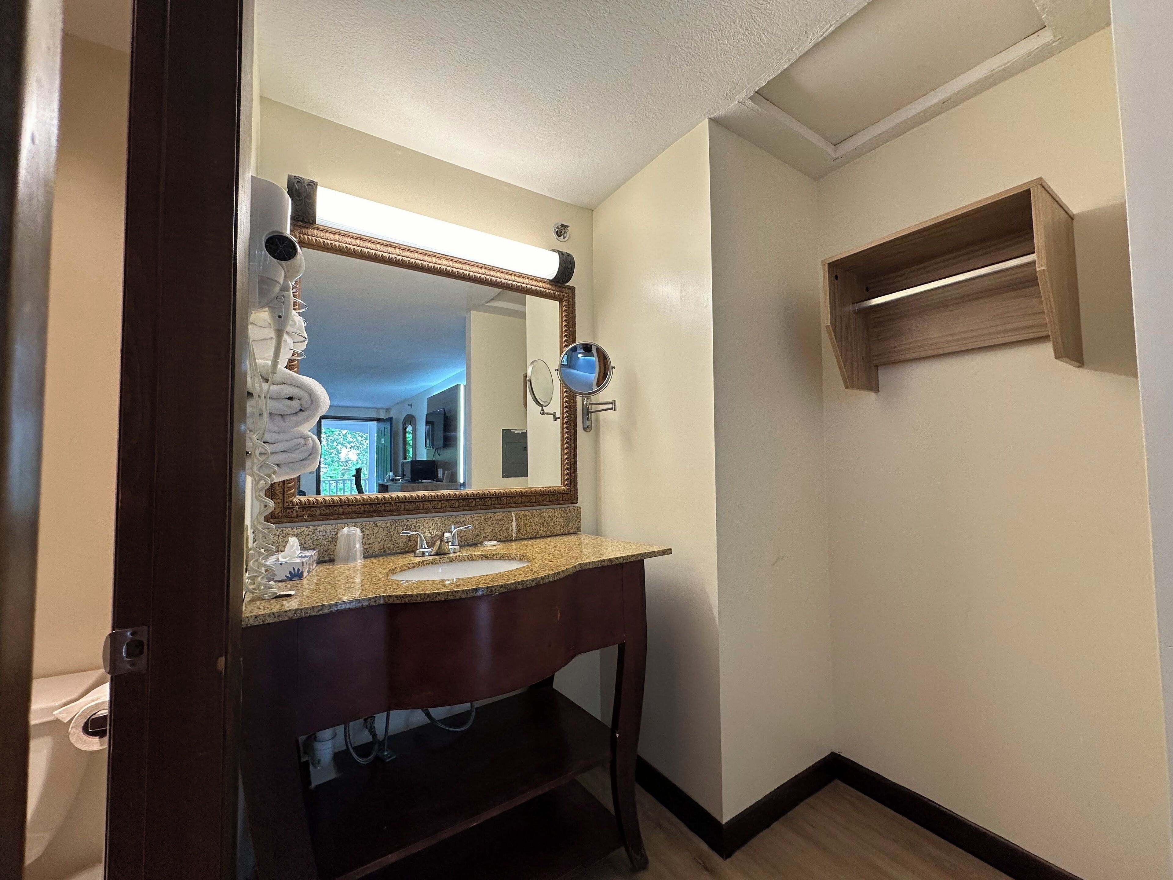 A bathroom with a wooden vanity, a large mirror, and a small shelf.