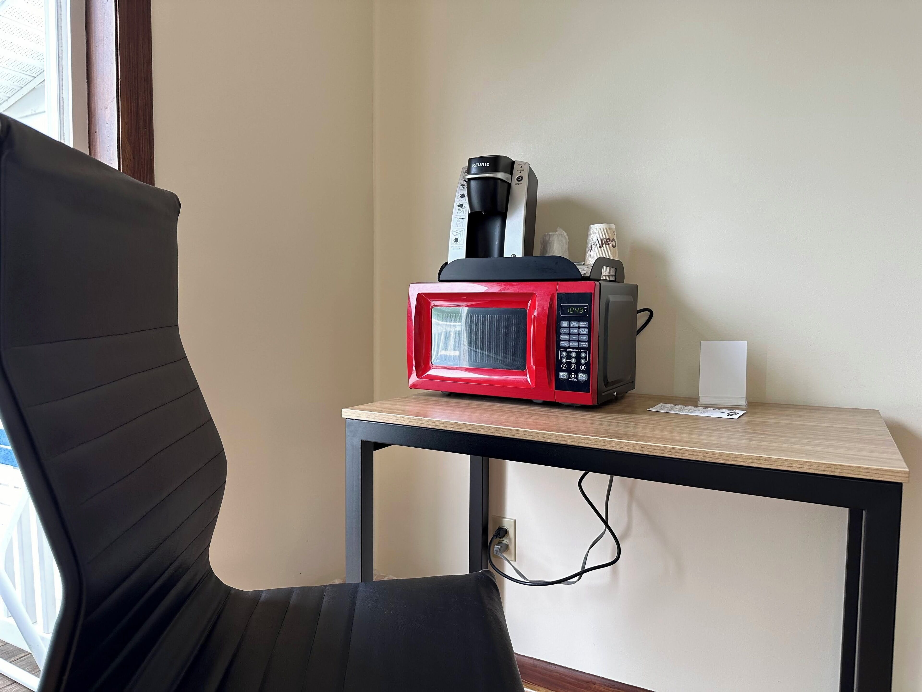 A kitchenette with a red microwave, a coffee maker, and a small white appliance on a wooden table.