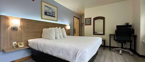 A hotel room with a bed, bedside lamp, telephone, and a desk with a chair.