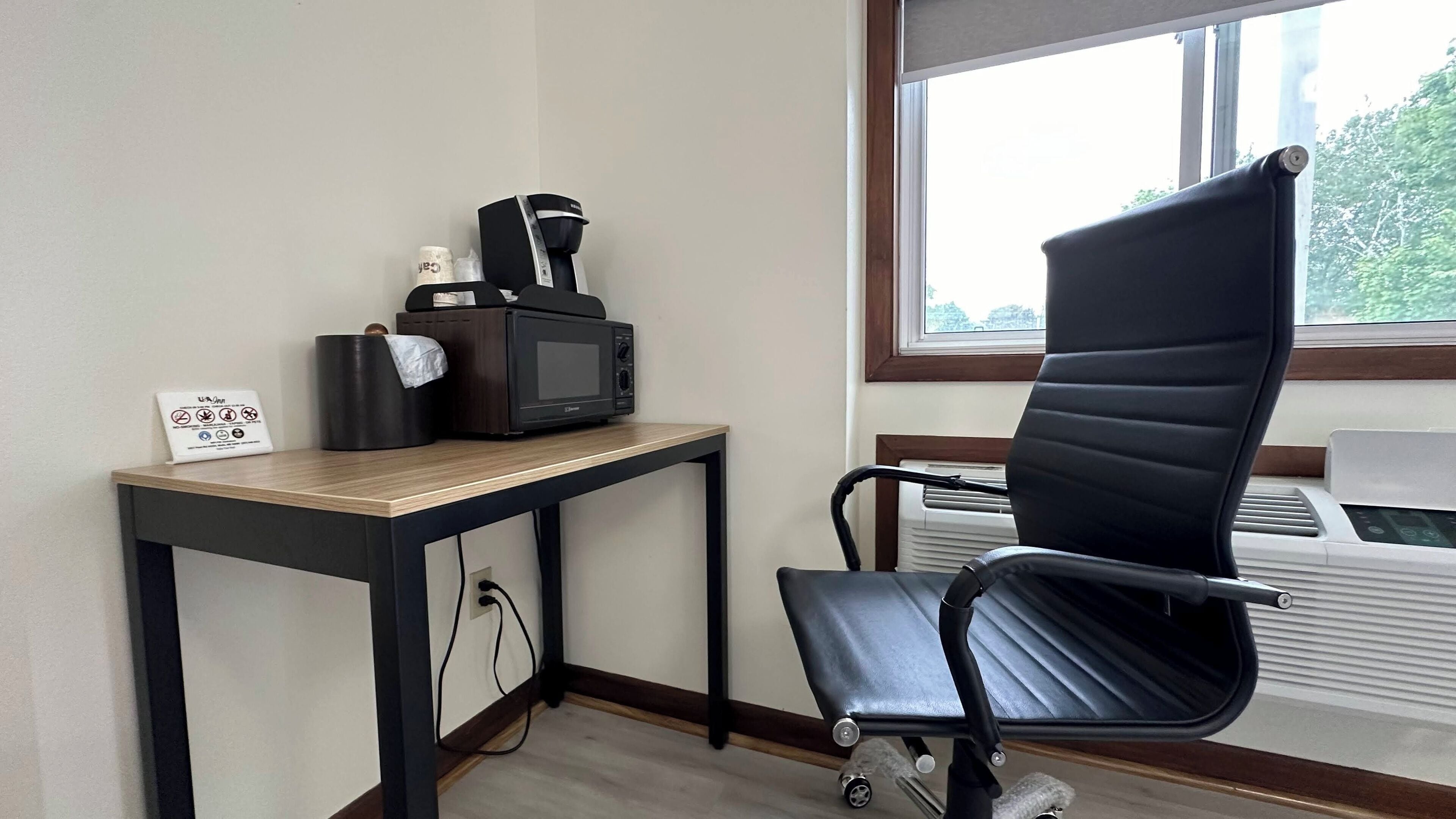 A small office space with a desk, a black office chair, a microwave, and a sign on the wall.