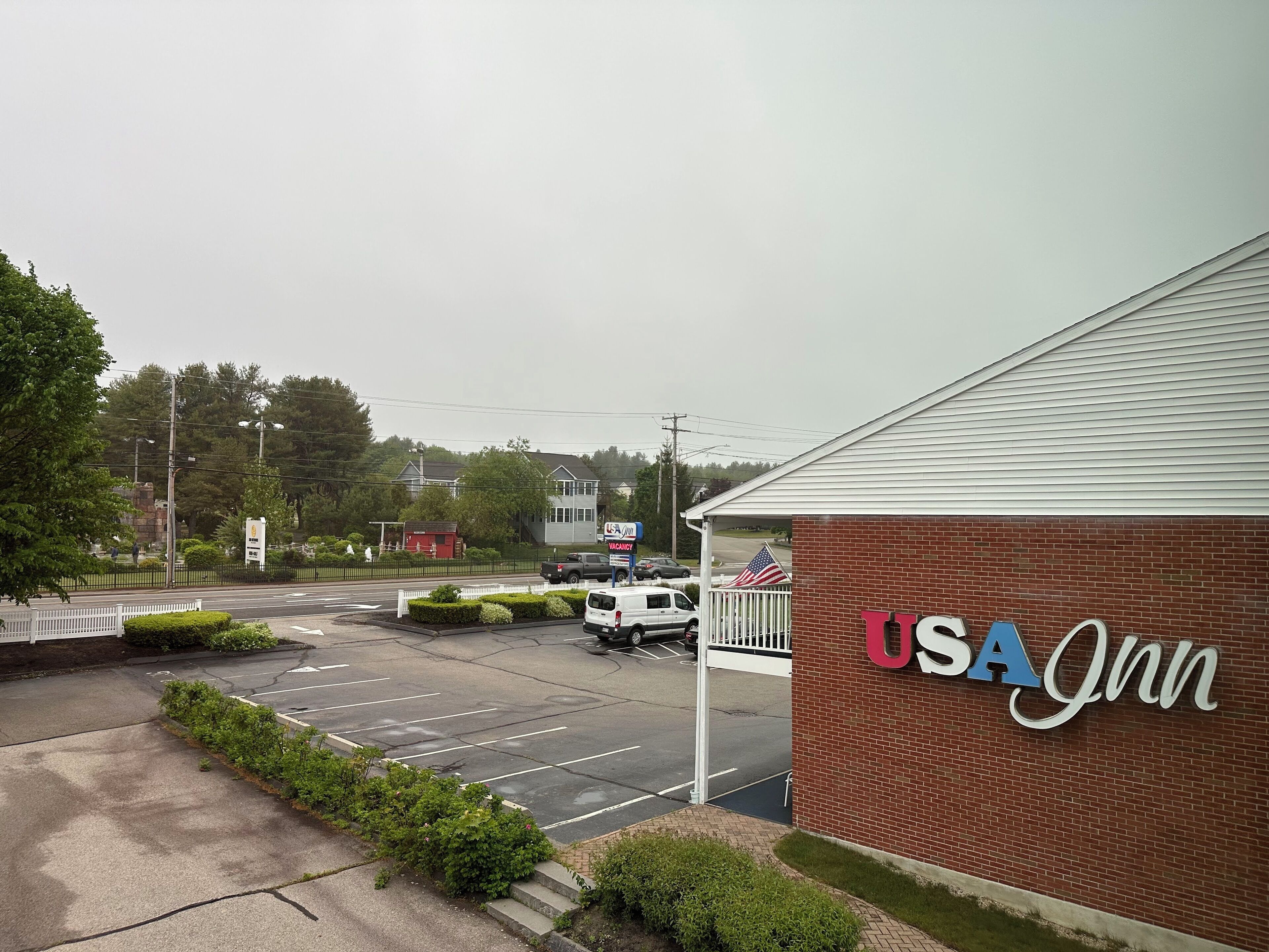 A USA Inn hotel with a brick facade, a parking lot, and a street view with cars and a flag.