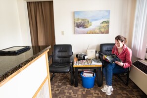 Una habitación con un escritorio, dos sillas, una mesa con revistas, una radio y un balde con objetos.