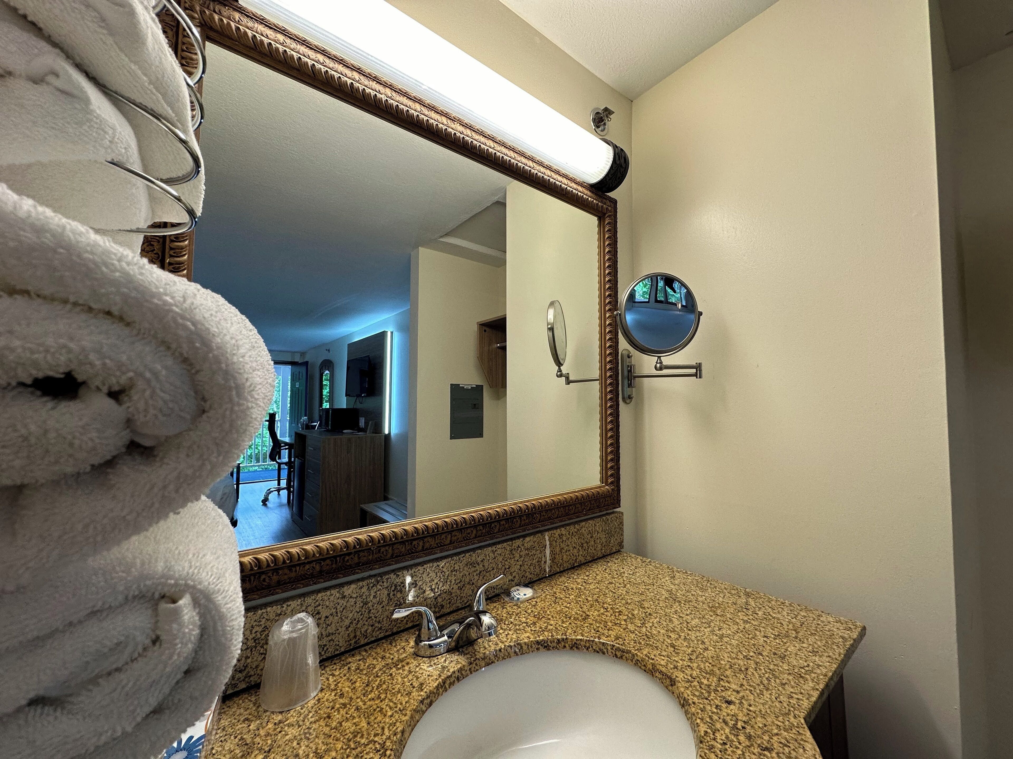 A bathroom with a granite countertop, a white sink, a large mirror, and a towel rack.