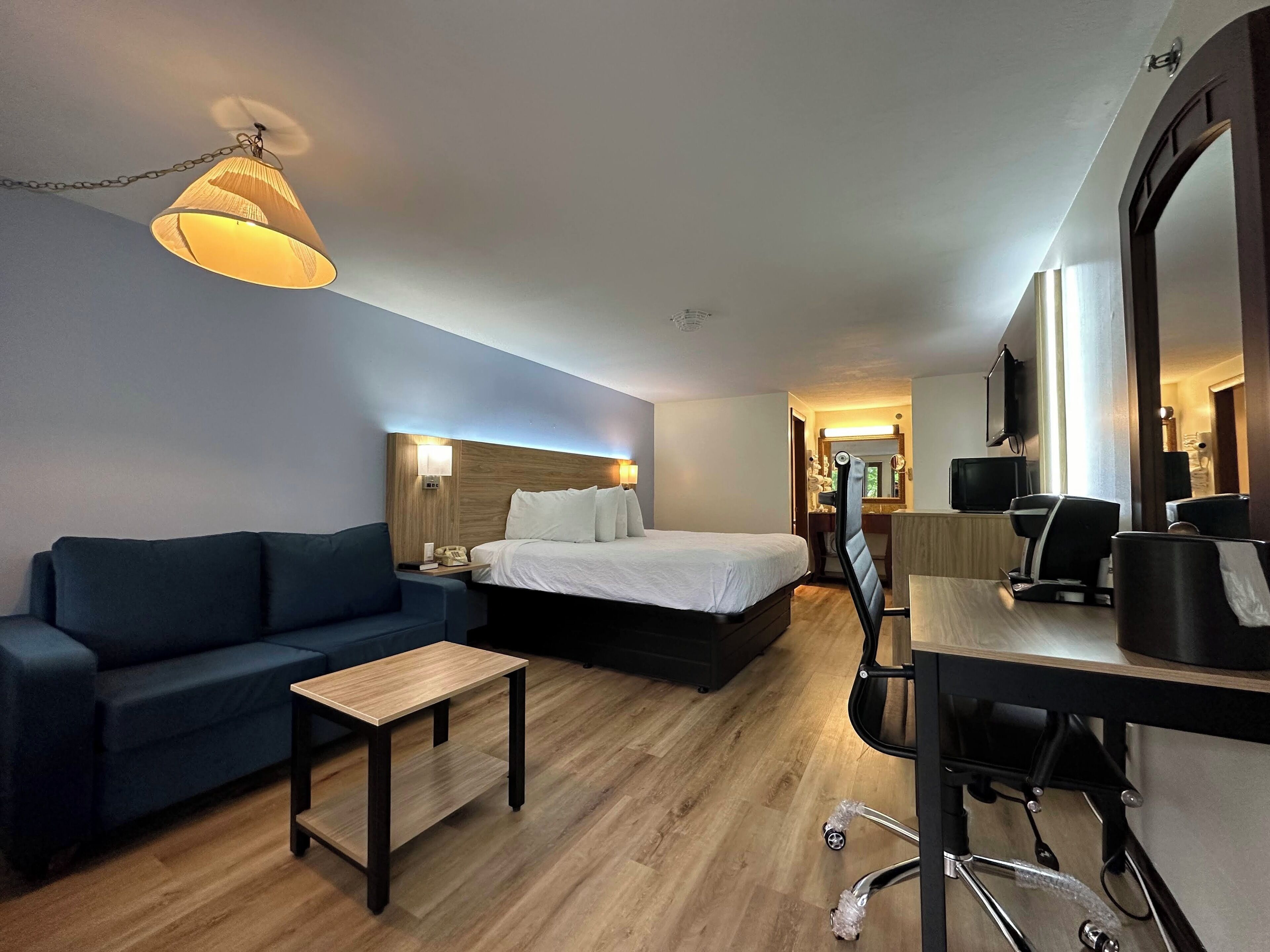 A hotel room with a bed, a desk, a chair, a sofa, and a lamp.