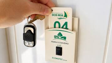 A hand inserting a key into a lock, with a label that reads 'RESIDENCIAL DOS REIS' and 'ECONOTECC.eco.br' on a beige wall.