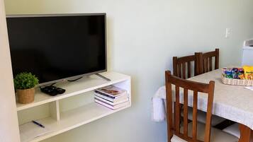 A dining area with a table, chairs, a TV on a shelf, and a 'PROIBIDO FUMAR' sign.