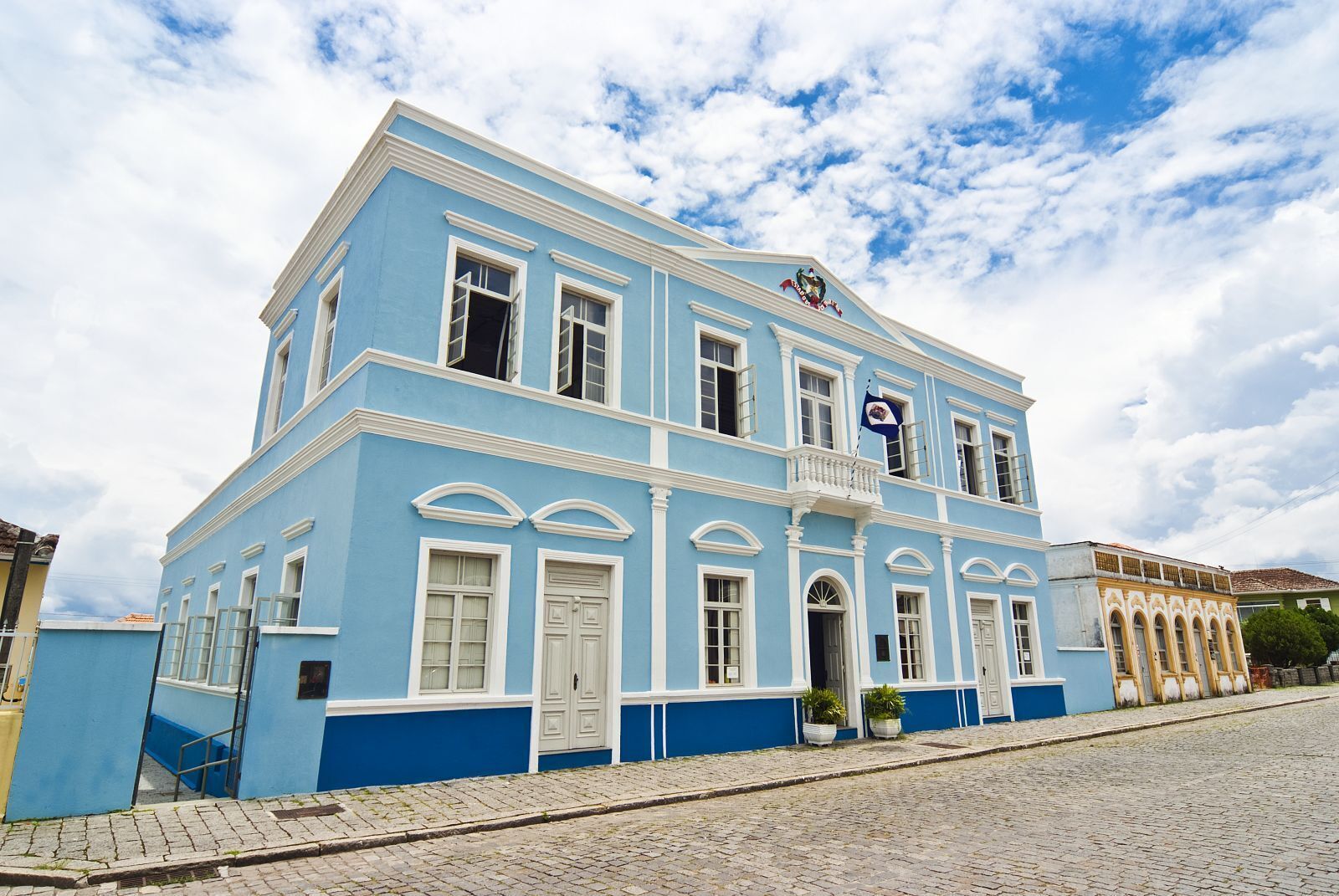 Un edificio de dos pisos con fachada azul, detalles blancos y un balcón.