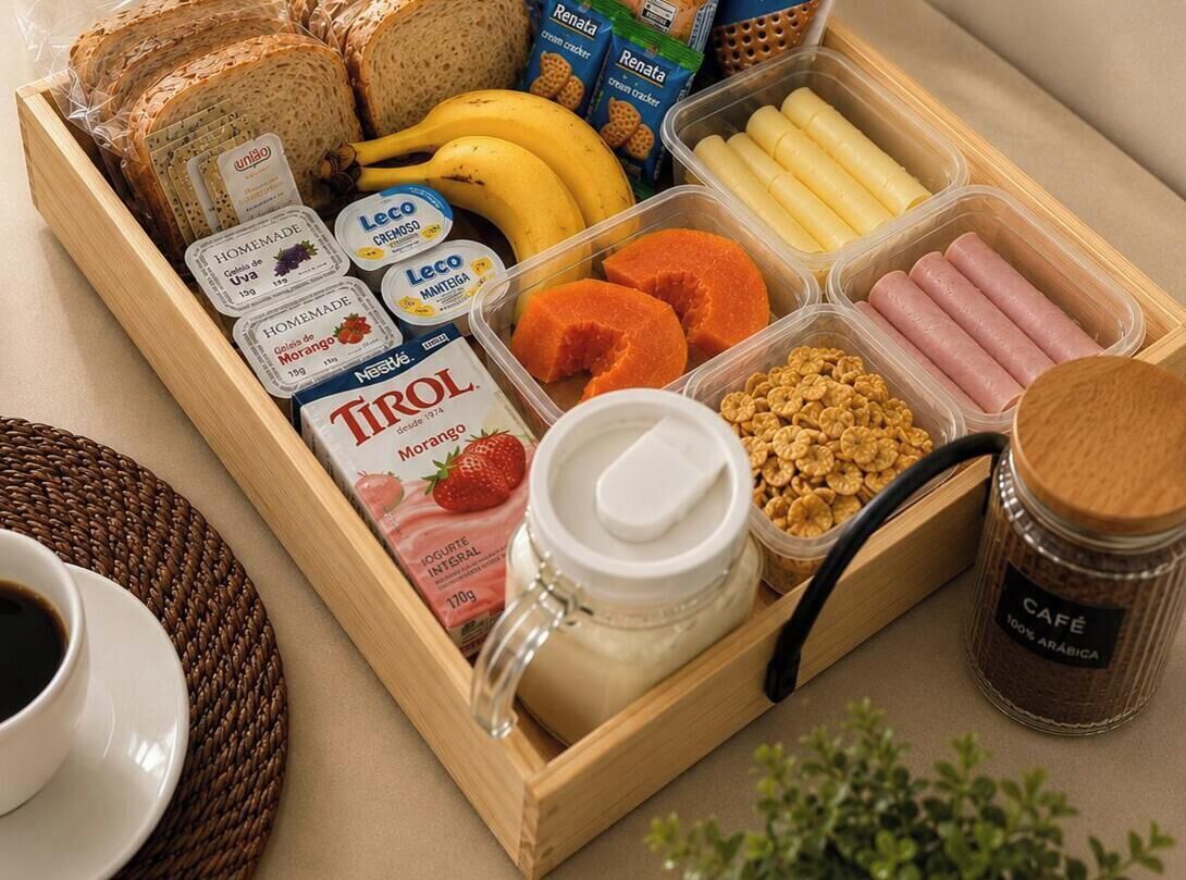 Un safata de fusta amb articles per esmorzar, com ara pa, plàtans, iogurt i cereals.