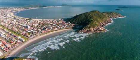 An aerial view of a coastal town with a beach, residential area, and a prominent green hill.