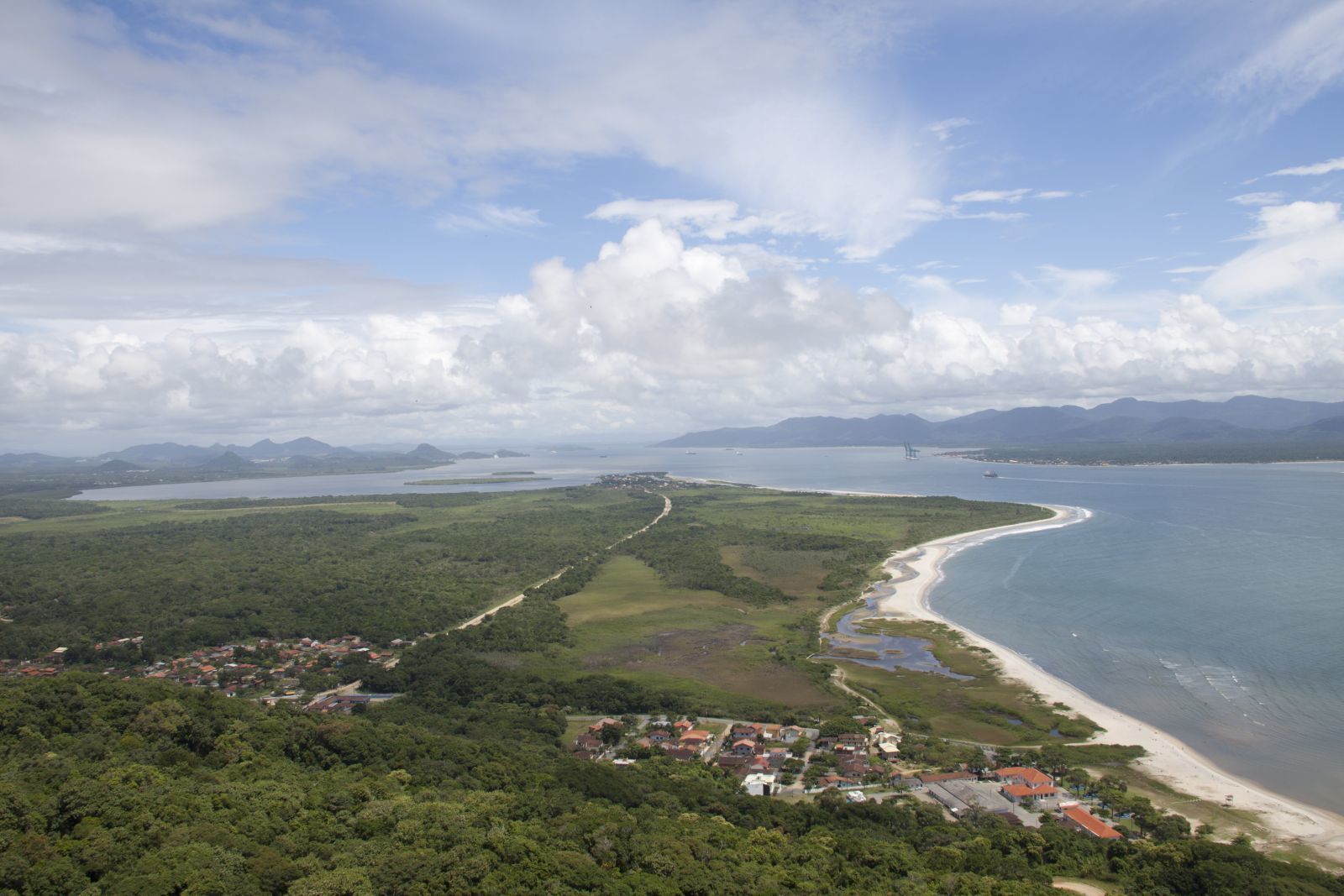 Vue aérienne d’une zone côtière comprenant une plage, une route et une zone boisée.