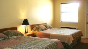 A room with two beds, a nightstand with a lamp, and a window with blinds.