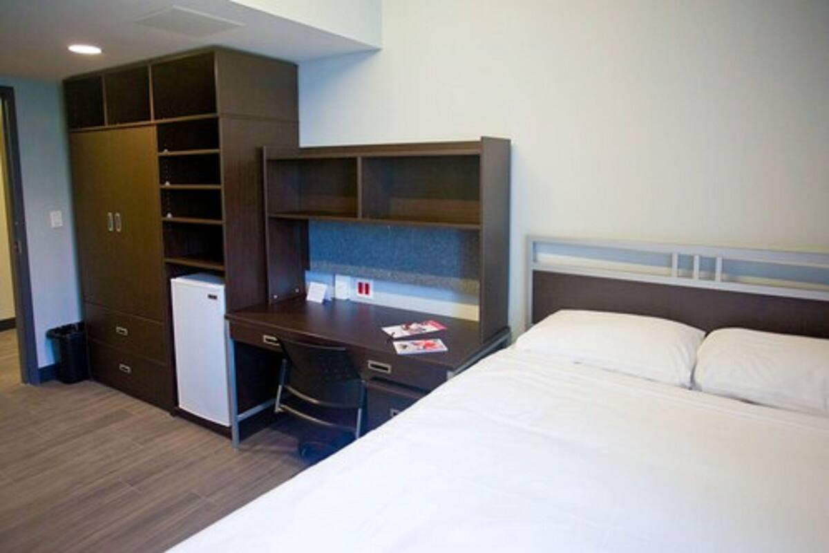 Een hotelkamer met een bed, een bureau met stoel, een kleine koelkast en een kledingkast.