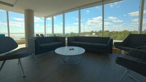 A modern lounge with a large window offering a view of the sea and greenery. - Queen's University - David C. Smith House - Campus Accommodation (Kingston)