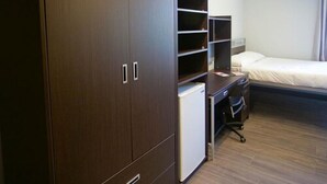 A hotel room with a wardrobe, a desk with a chair, a bed, and a small white refrigerator. - Queen's University - David C. Smith House - Campus Accommodation (Kingston)