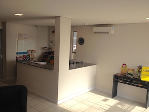 Ein Küchenbereich mit Kühlschrank, Spüle und einer Uhr an der Wand. Auf einem kleinen Tisch liegen eine gelbe Tasche und einige Gegenstände.