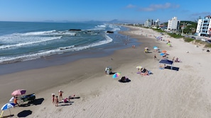 A beach with a wide sandy shore, umbrellas, and beach chairs.