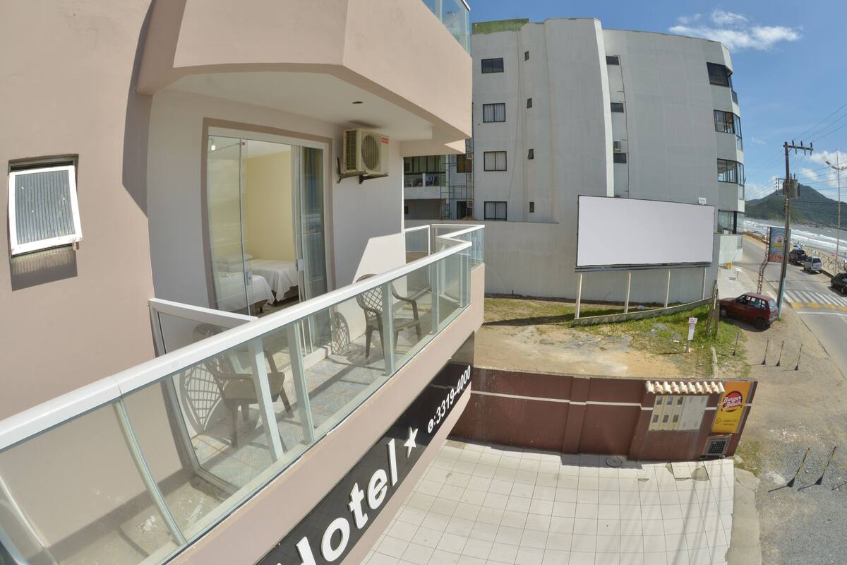 A hotel with a glass balcony, a visible room with a bed, and a signboard.