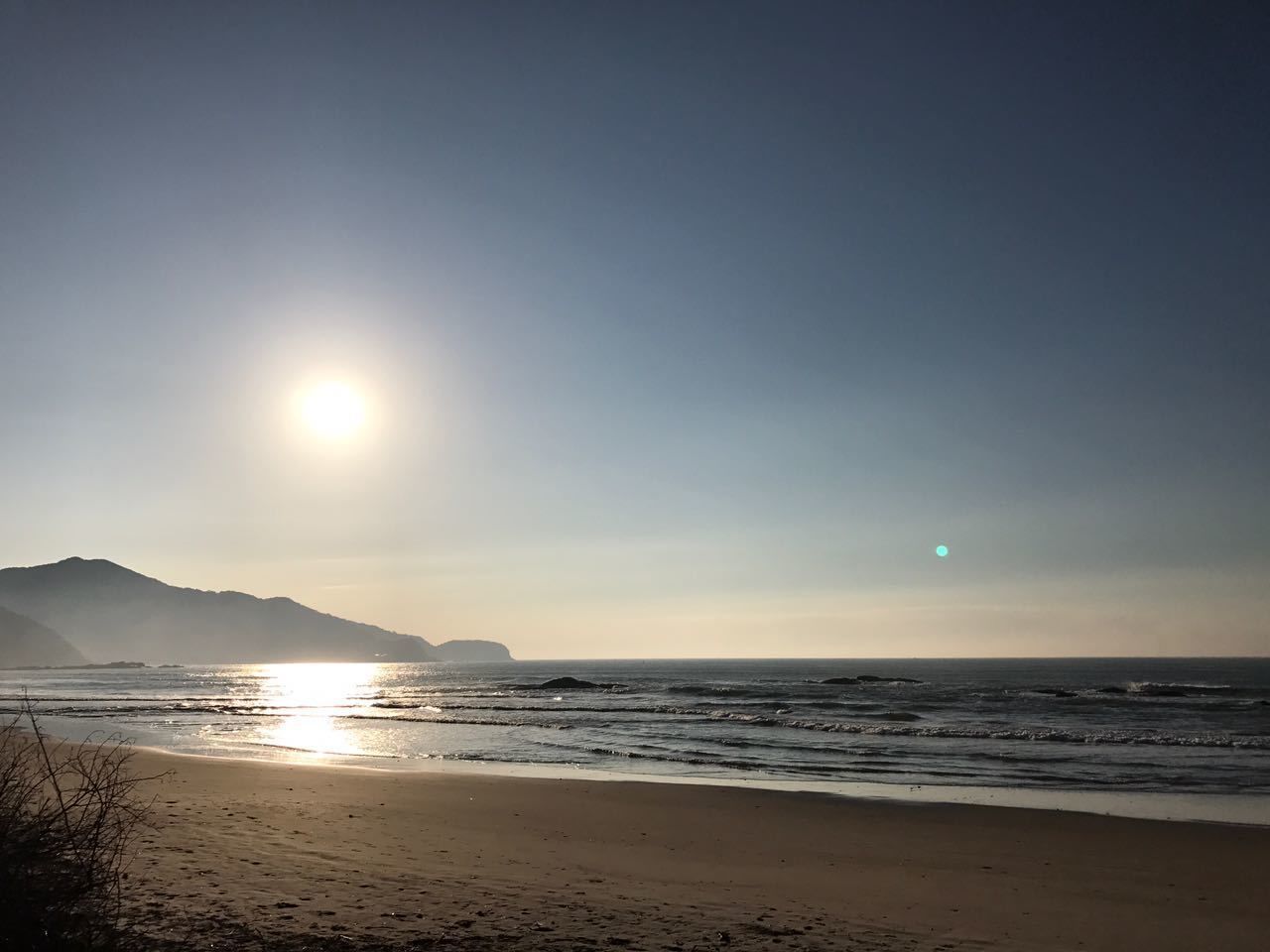 A beach with the sun low on the horizon, casting a warm glow on the sand and water.
