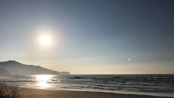 A beach with the sun low on the horizon, casting a warm glow on the sand and water.
