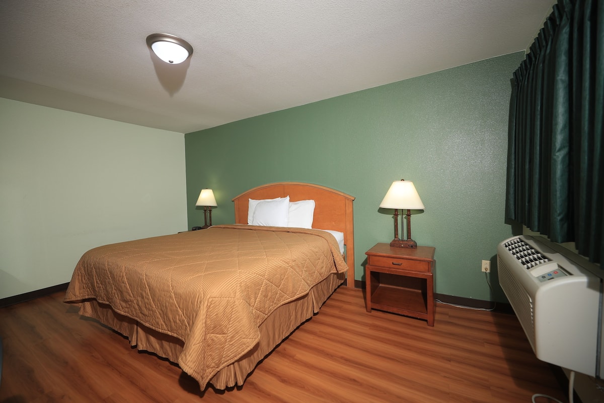 Ein Hotelzimmer mit einem großen Bett, zwei Nachttischen mit Lampen, einem Heizkörper und einem Fenster mit Vorhängen.