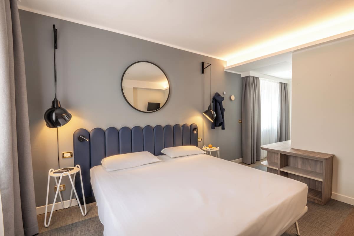 A hotel room with a bed, bedside tables, a mirror, and a desk.