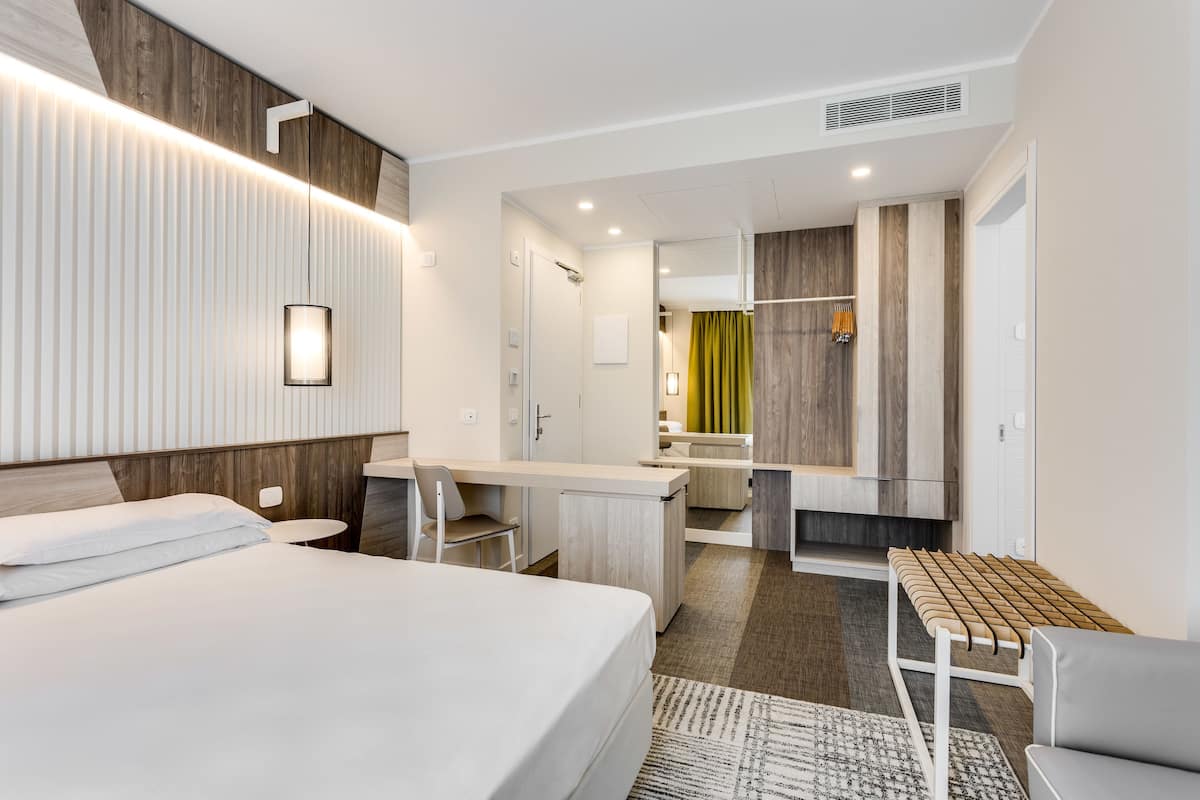 A modern hotel room with a bed, desk, and seating area.
