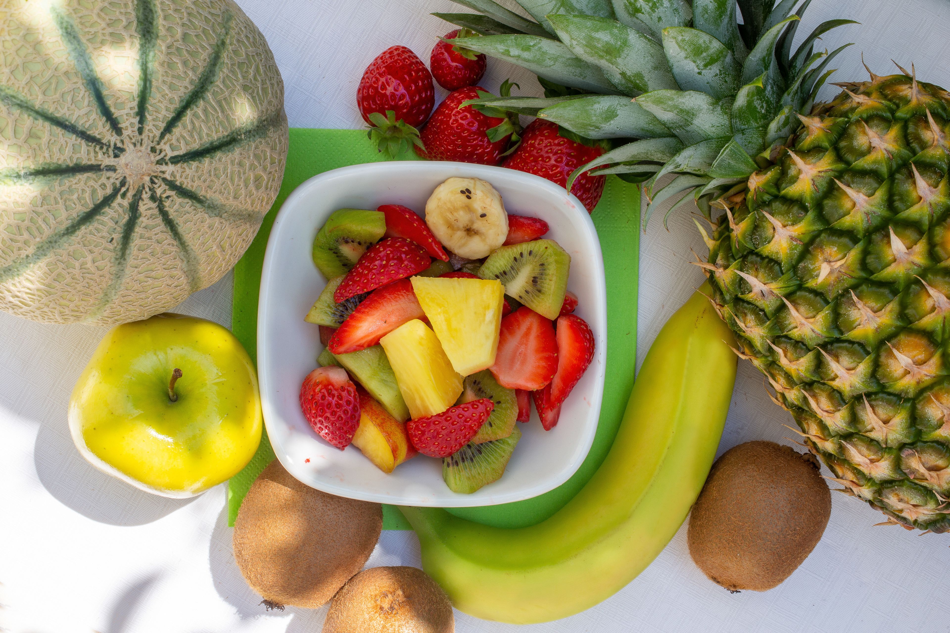 A variety of fruits including a melon, pineapple, kiwi, strawberries, bananas, and an apple.