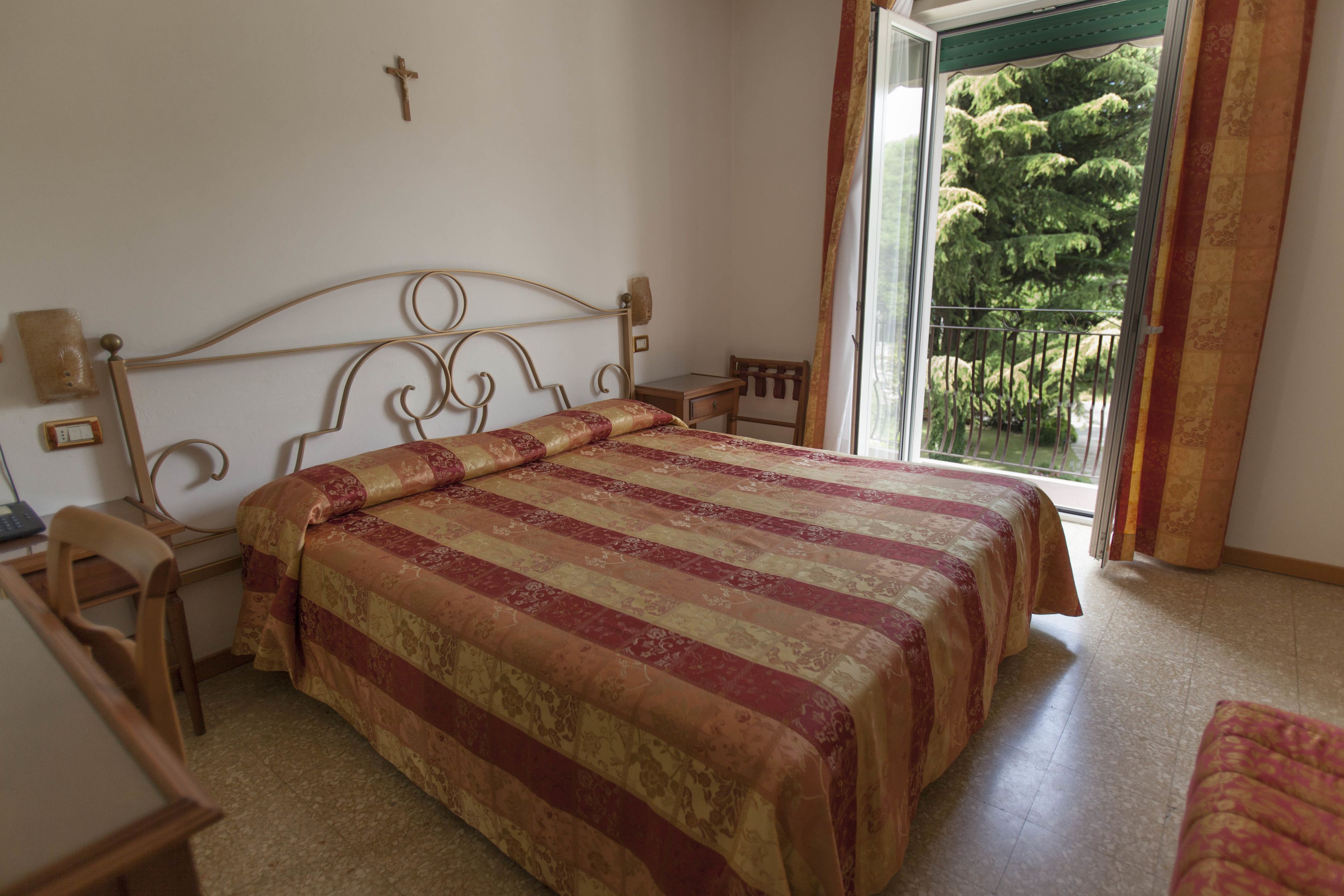 A bedroom with a bed, a desk, and a chair. There is a window with a view of trees.