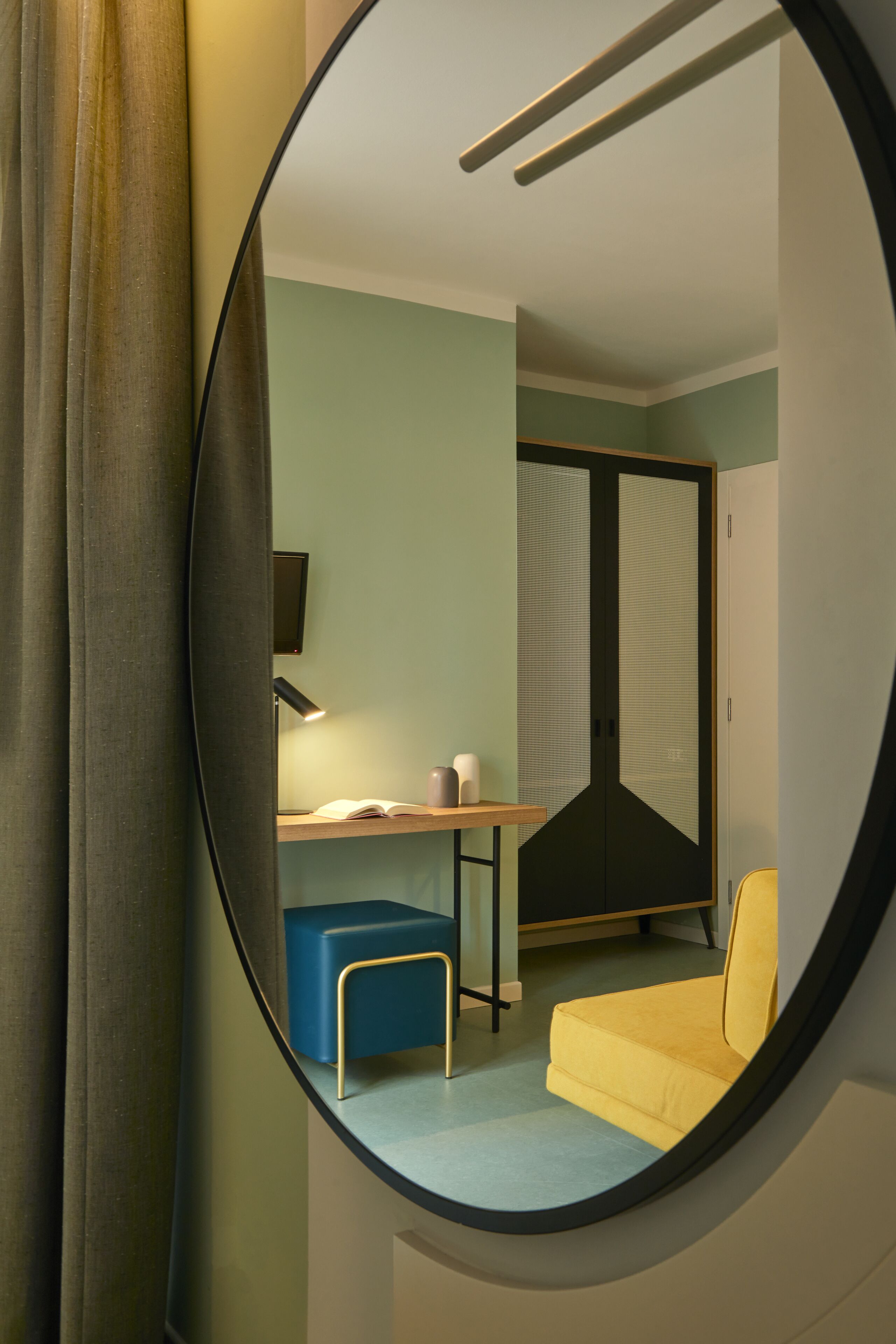 A room with a round mirror reflecting a desk, chair, and a wardrobe.
