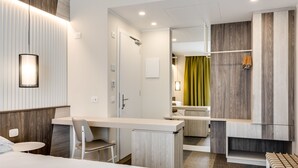A modern hotel room with a bed, a desk, a chair, and a bathroom visible through an open door. - Hotel Europa (Garda)