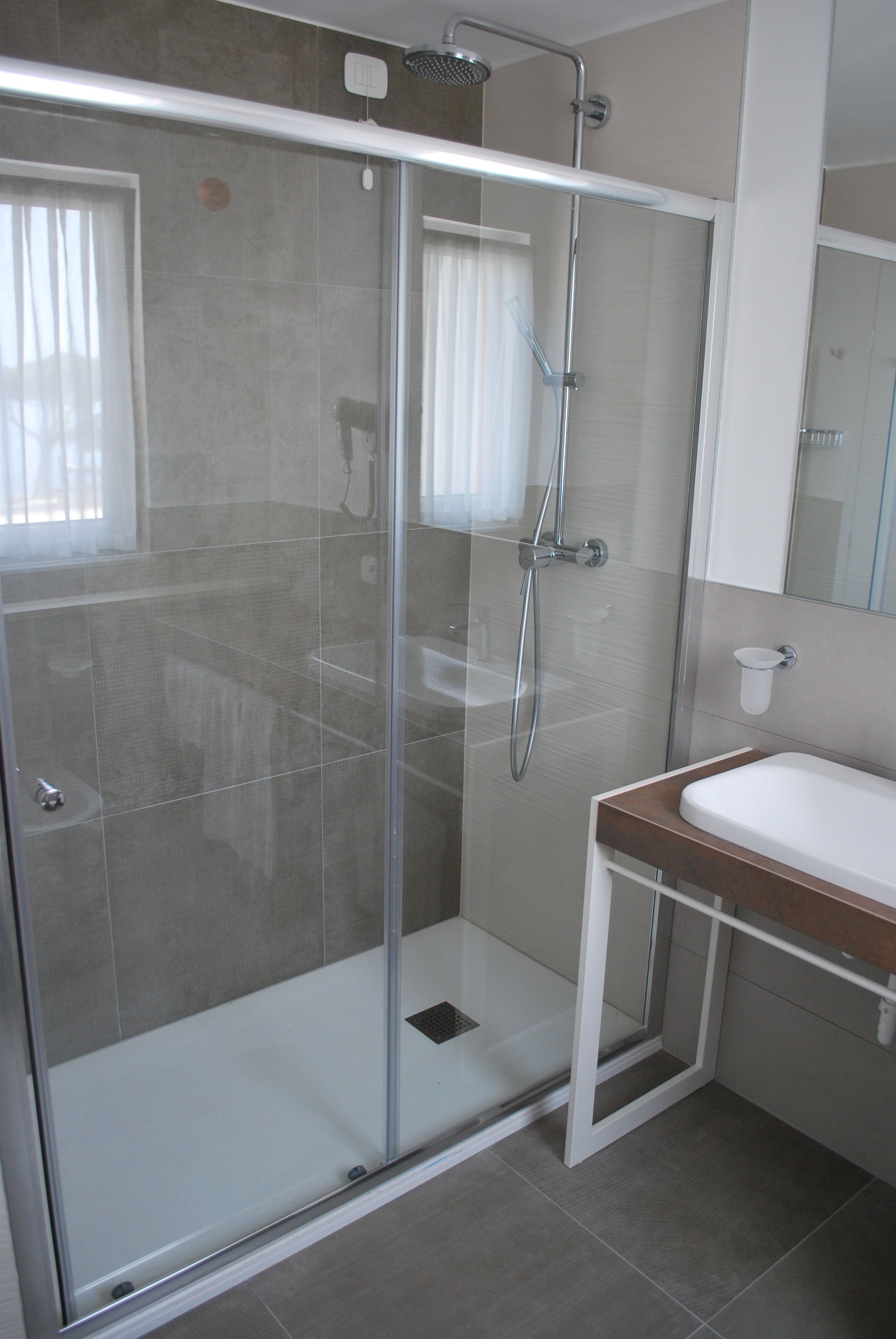 Un baño moderno con ducha de mampara de vidrio, un lavamanos blanco y un espejo sobre él.
