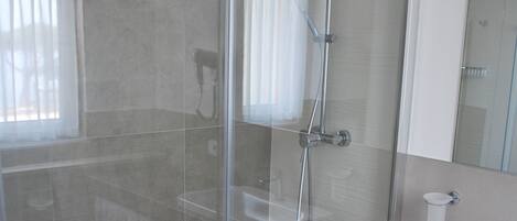 Un baño moderno con ducha de mampara de vidrio, un lavamanos blanco y un espejo sobre él.