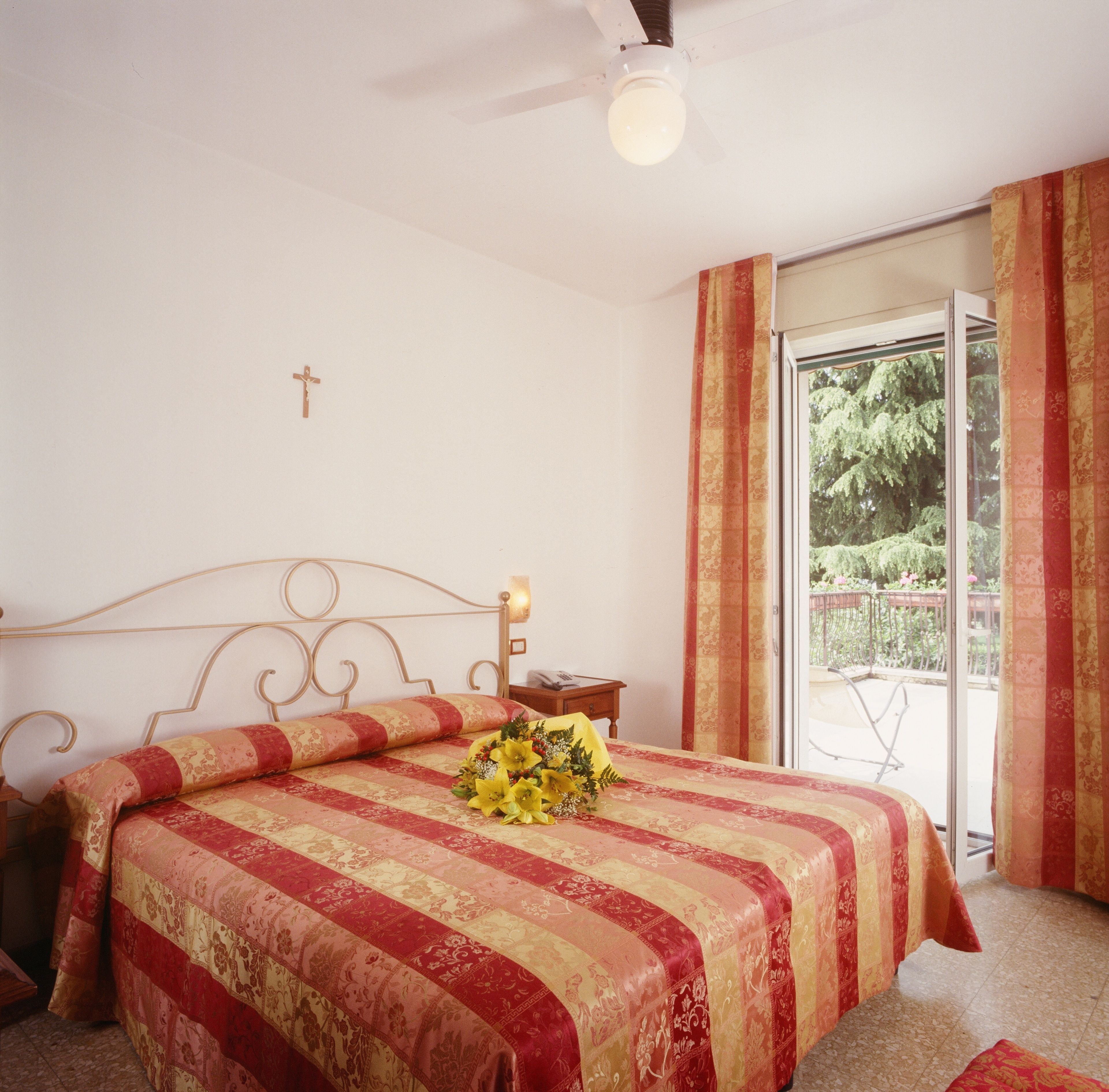 A bedroom with a bed, a cross on the wall, and a balcony with curtains.