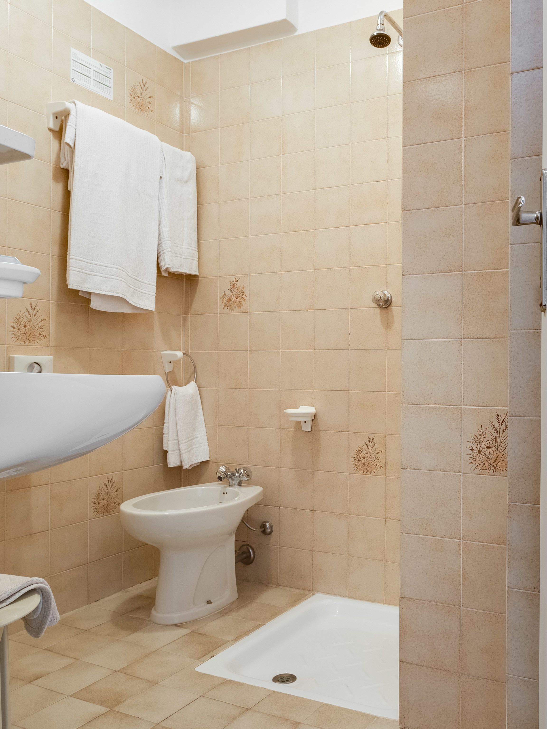 A bathroom with beige tiles, a sink, a bidet, and a shower.