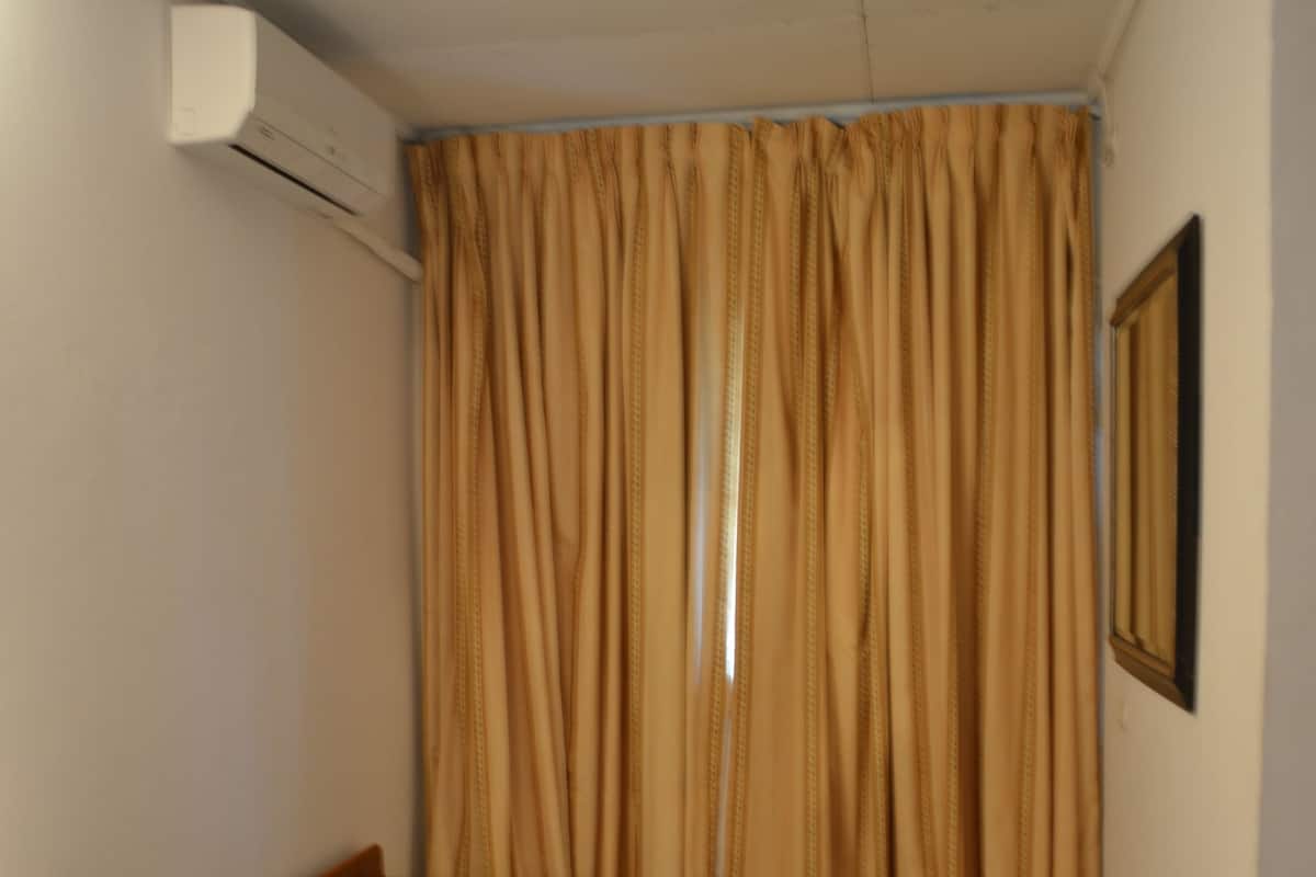 A small room with a bed, a table, and an air conditioning unit.
