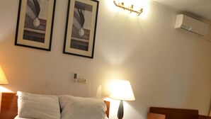 A hotel room with a bed, two framed pictures on the wall, a bedside lamp, and an air conditioning unit. - L'Aquarius Marina 2000 (Douala)