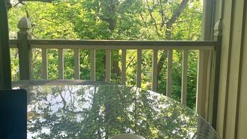 A glass table with a cup on it, surrounded by a white railing, with trees in the background.