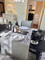 A dining table set with plates, cutlery, glasses, and a kettle, with striped tablecloths and a lamp in the background.