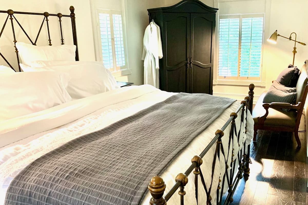 A bedroom with a large bed, a dark wooden wardrobe, and a chair.
