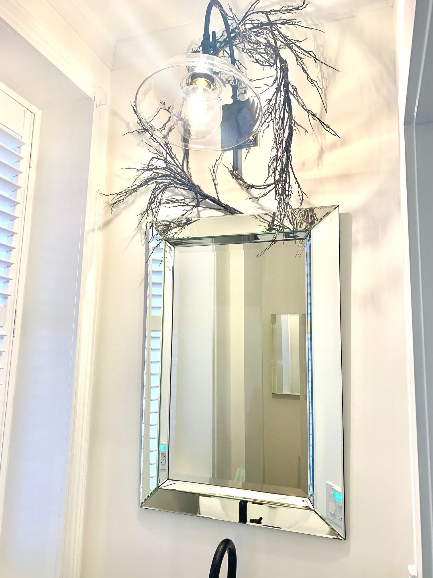 A bathroom with a rectangular mirror, a black sink, and a light fixture with branches.
