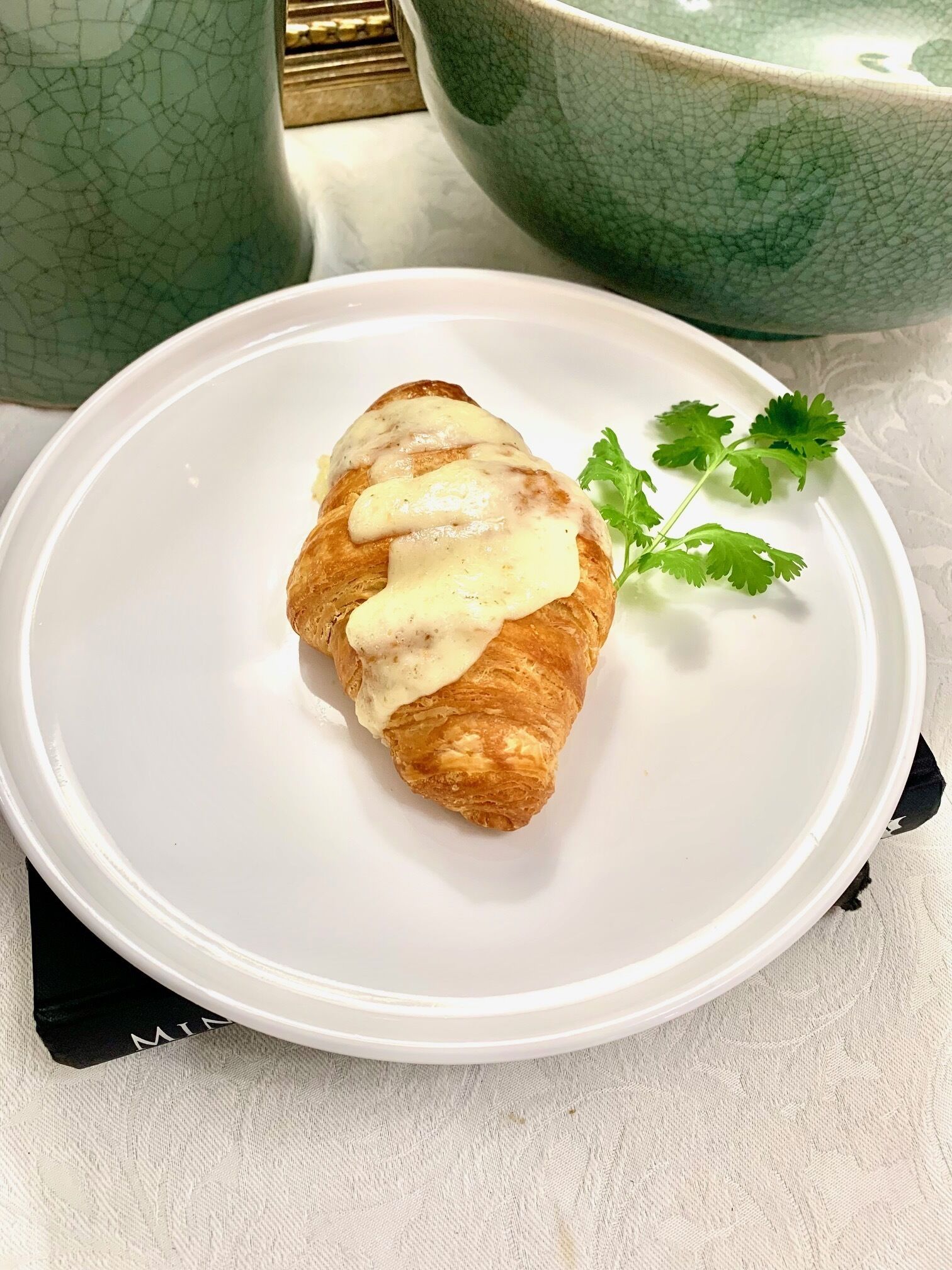 En tallrik med en croissant, täckt med en vit sås och garnerad med persilja, placerad på en vit tallrik.
